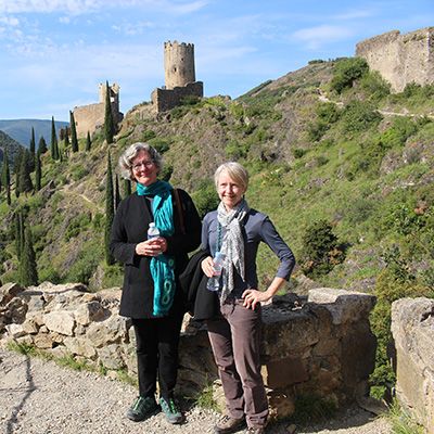 Two women professors are standing in front of castle ruins.